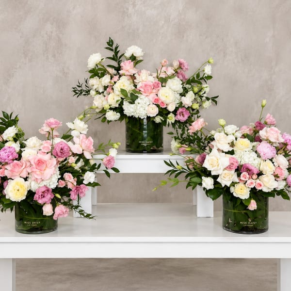 Three pastel floral arrangements in dark glass vases on white tables