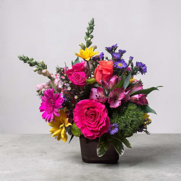 Mixed bouquet of bright roses, daisies, and lilies in a dark vase