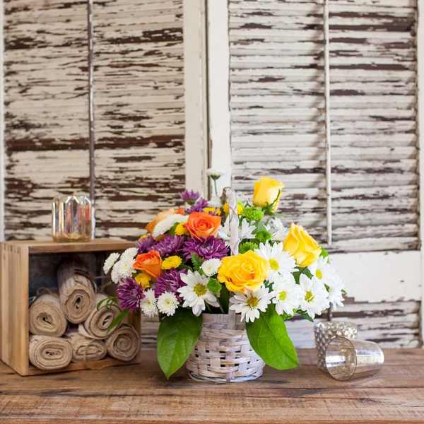 Basket arrangement of yellow and orange roses with white and purple daisies