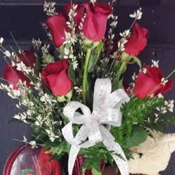 Red roses in a vase with a white ribbon and teddy bear