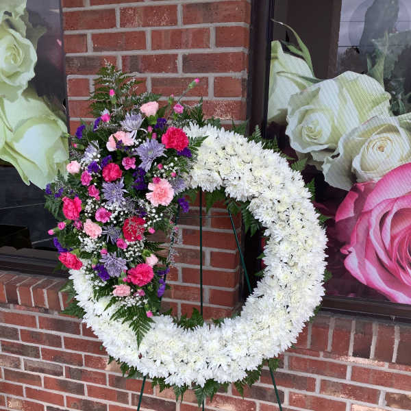 Heart-shaped floral wreath on a stand with white and mixed pink-purple flowers