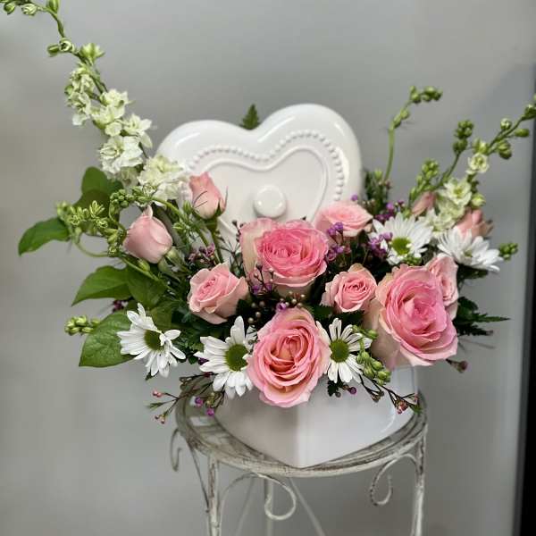 Pink roses and white daisies arranged in a white heart-shaped vase