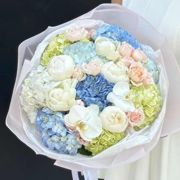 Pastel bouquet of hydrangeas, roses, and white orchids wrapped in pink paper