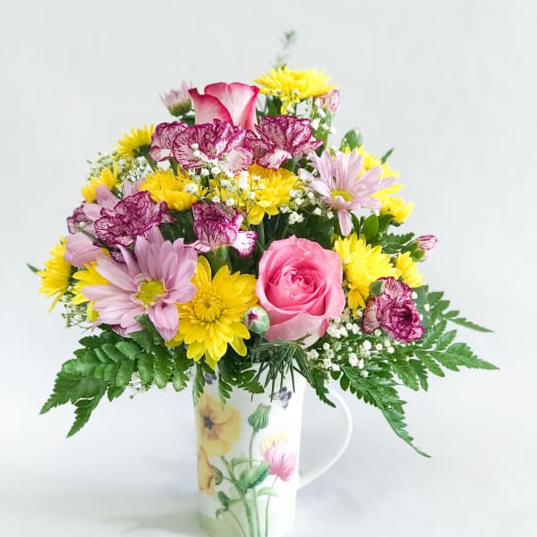 Mixed bouquet in a floral mug vase with pink, yellow, and purple blooms