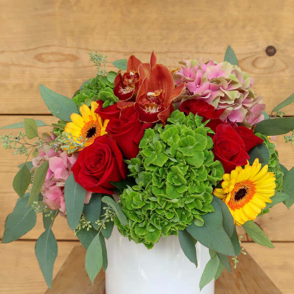 Bouquet of red roses, green hydrangea, and yellow gerbera daisies in a white vase