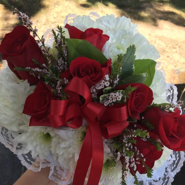 Red roses and white chrysanthemums in a lace-wrapped bouquet with a red ribbon