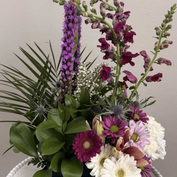 Mixed floral arrangement with purple and white blooms in a black container