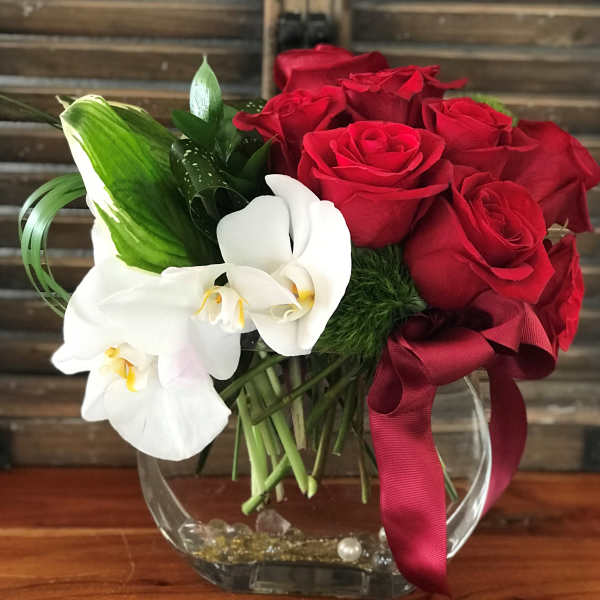 Red roses and white orchids in a clear glass vase with a burgundy ribbon