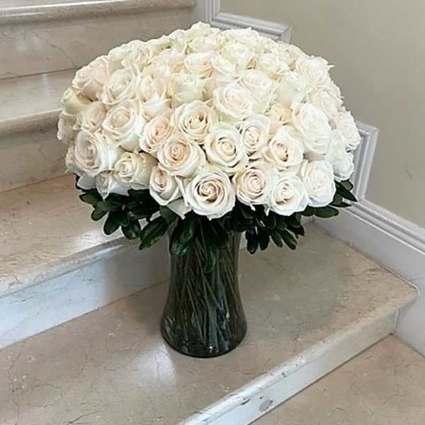 Large arrangement of white and cream roses in a clear glass vase on marble steps