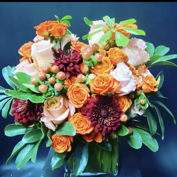 Bouquet of orange and white roses with dark burgundy blooms in a glass vase