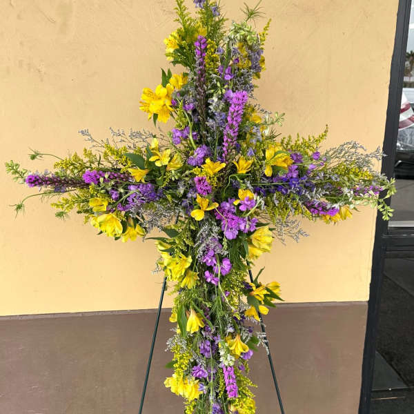 Tall floral cross on an easel with yellow and purple flowers
