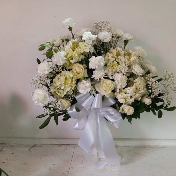 White floral standing spray with a large white ribbon bow