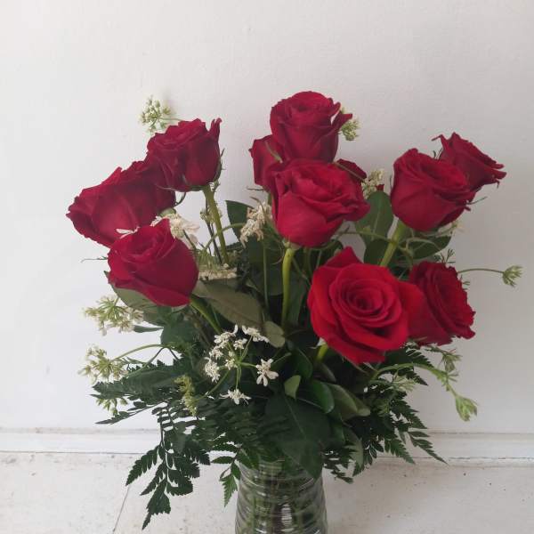 Red roses arranged in a clear glass vase with white filler flowers