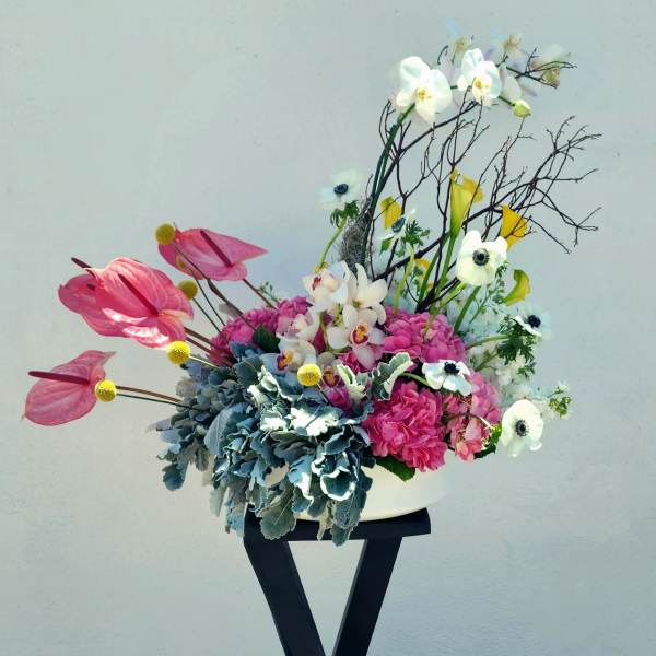 Pink and white floral arrangement in a white vase on a black stand