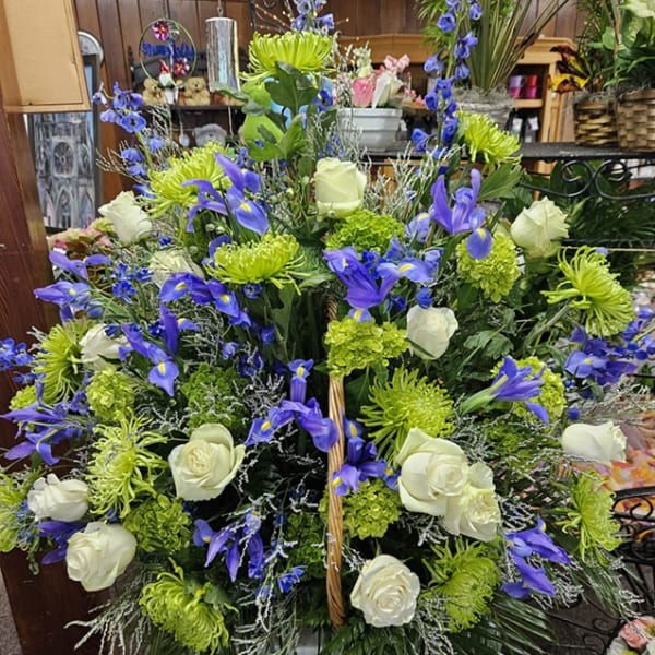 Tall blue iris, green mums, and white rose arrangement in a white pedestal vase