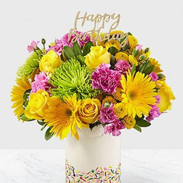 Bright mixed bouquet in a white vase with a gold "Happy" topper