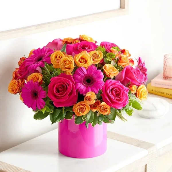 Pink and orange mixed flower arrangement in a bright pink vase