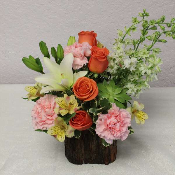 Mixed bouquet with orange roses, pink carnations, white lilies, and white filler flowers in a wood container