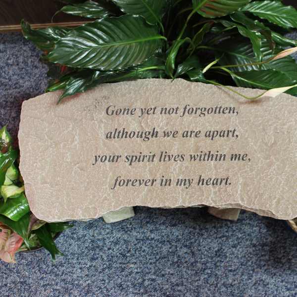 Memorial stone with engraved text surrounded by green plants