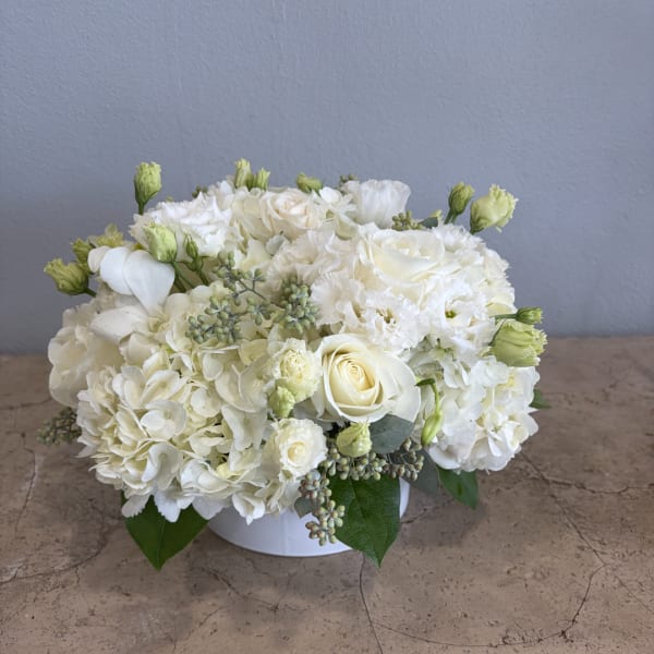 White floral arrangement in a low round vase with roses and hydrangeas