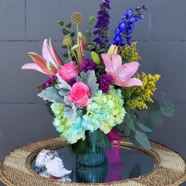 Colorful bouquet of lilies, roses, hydrangeas, and delphinium in a glass vase