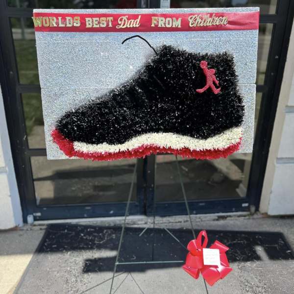 Black sneaker-shaped floral tribute on a stand with a red bow