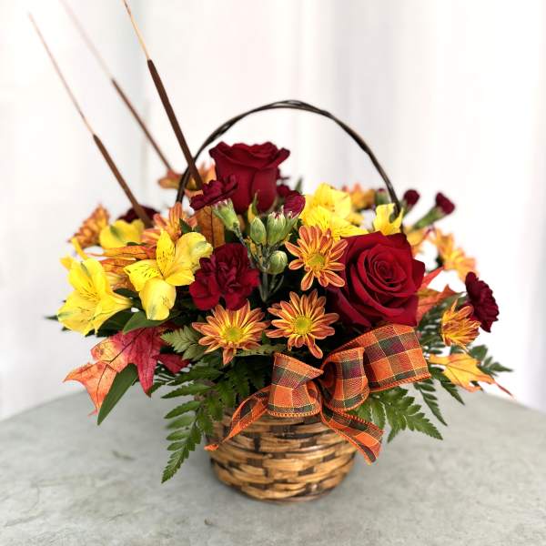 Basket arrangement of red roses and yellow flowers with an autumn ribbon
