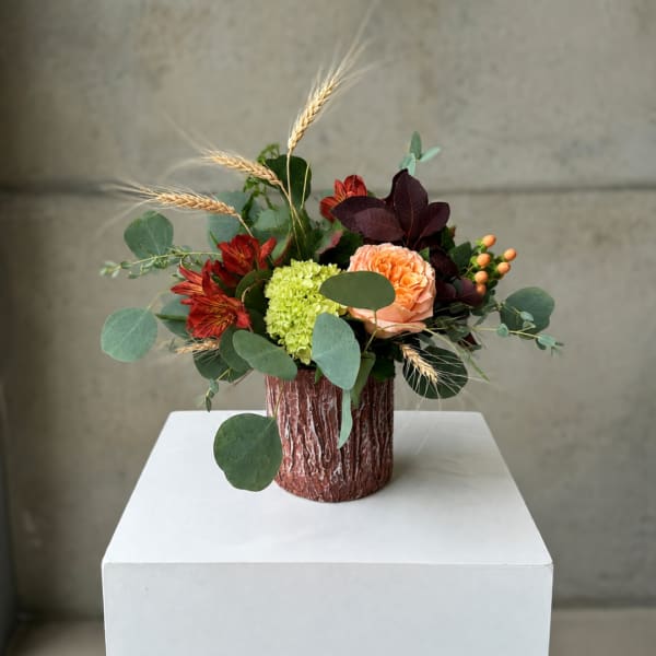 Mixed bouquet in a textured brown vase with peach, red, and green blooms