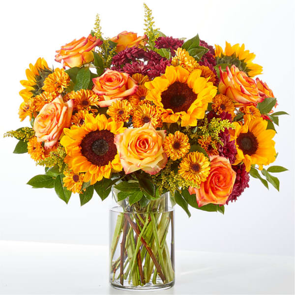 Bouquet of sunflowers, orange roses, and burgundy mums in a clear glass vase