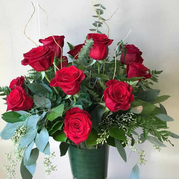 Red roses arranged in a clear glass vase with greenery