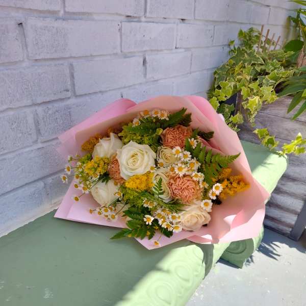 Bouquet of cream roses, peach carnations, and small white daisies in pink wrap