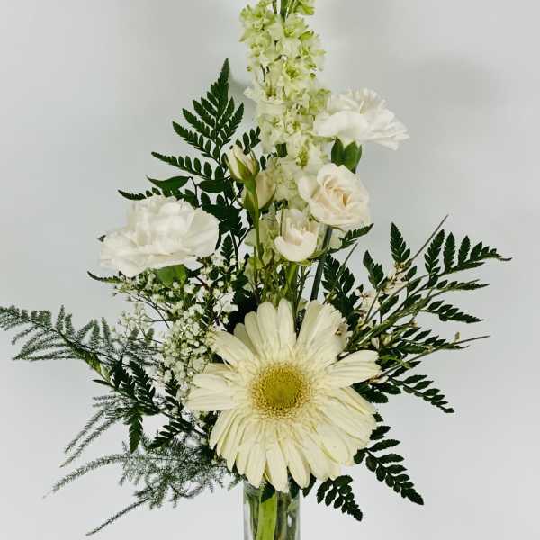 White flowers arranged in a tall glass vase with dark greenery
