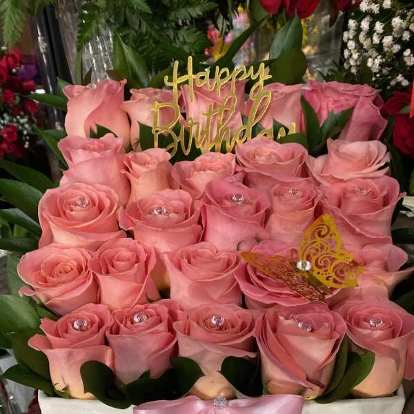 Pink roses arranged in a white box with a pink ribbon and birthday topper
