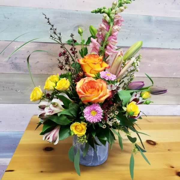 Mixed bouquet in a gray vase with orange roses, yellow spray roses, and pink blooms