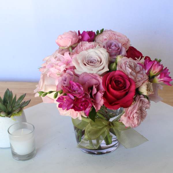Pink and red rose bouquet in a glass vase beside a small succulent and candle