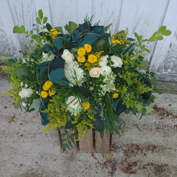 Large floral arrangement with white roses, yellow blooms, and dark green ribbon