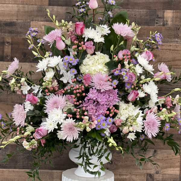 Large pink, white, and lavender floral arrangement in a white pedestal vase.