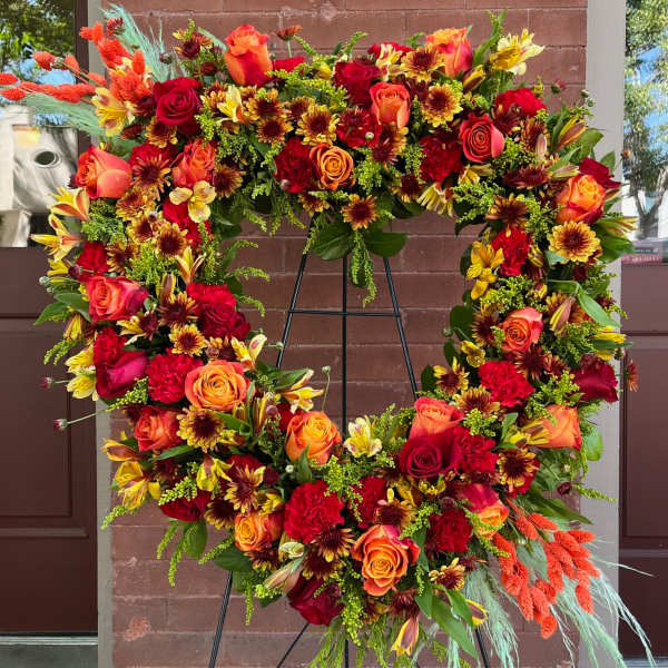 Large floral wreath with red, orange, and yellow blooms on a black stand
