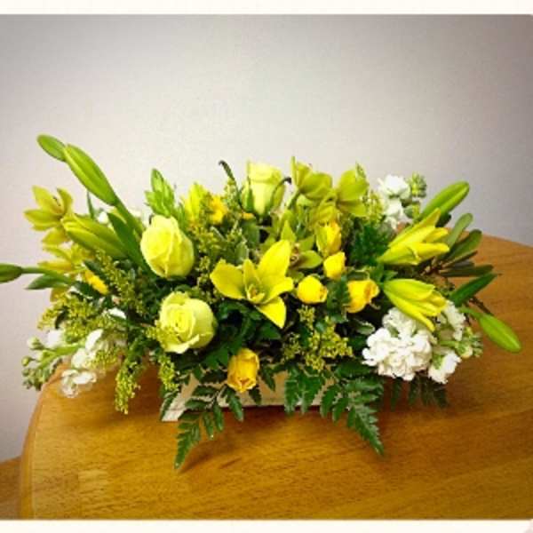 Yellow lilies and roses arranged with white flowers in a low centerpiece