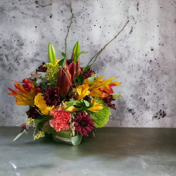 Autumn floral arrangement with lilies, roses, and mums in a low container