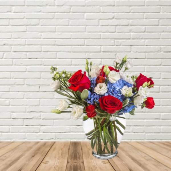 Bouquet of red roses, blue hydrangeas, and white blooms in a glass vase