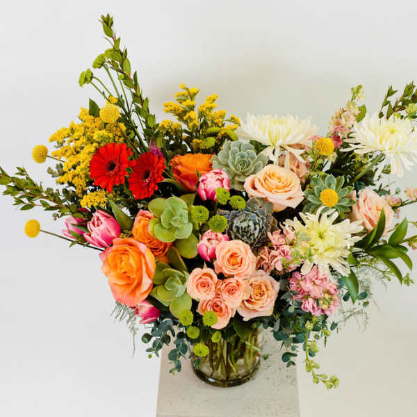 Mixed bouquet of roses, gerbera daisies, and succulents in a glass vase