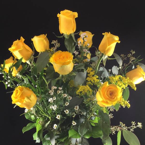 Yellow roses in a clear glass vase with mixed greenery