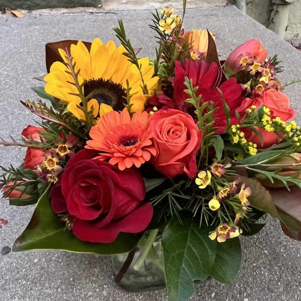 Bouquet of sunflowers, roses, and gerbera daisies in a glass vase