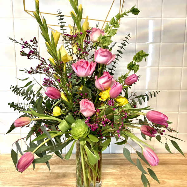 Tall mixed bouquet with pink roses, pink tulips, and yellow blooms in a glass vase