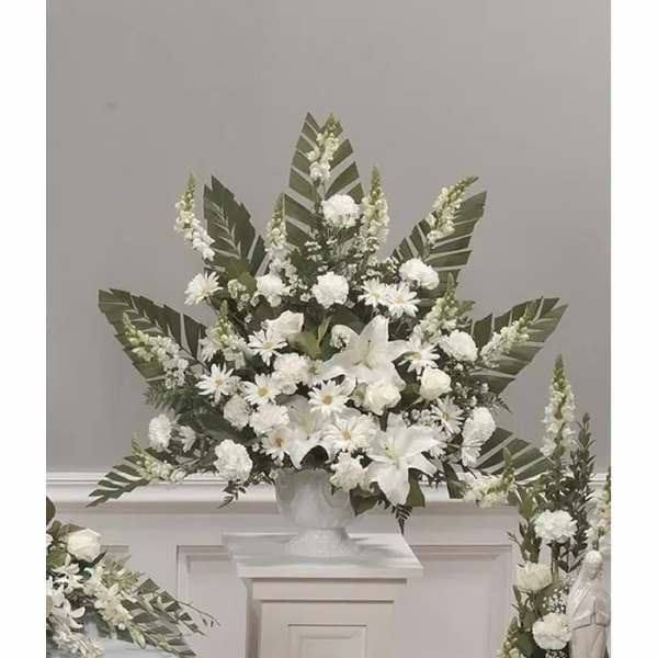White floral arrangement in a white urn with large green leaves