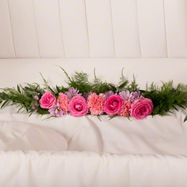 Pink roses and carnations arranged with greenery on a white couch