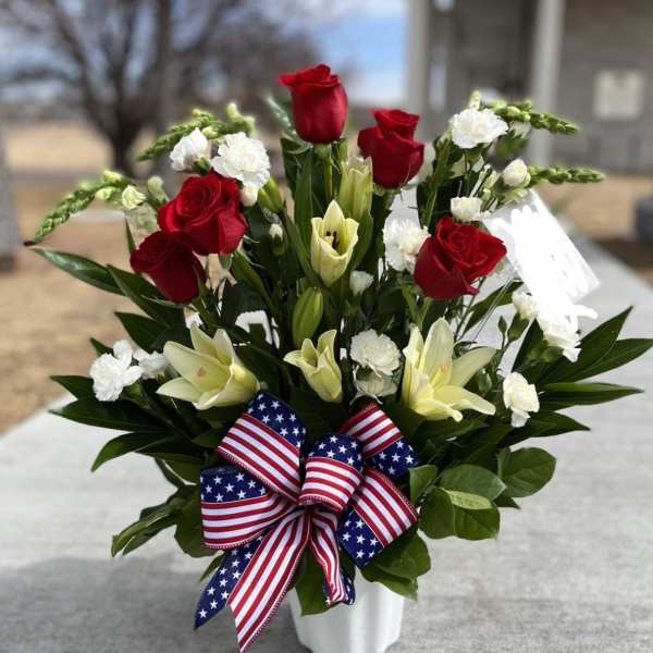 Red roses and white lilies in a white vase with an American flag ribbon