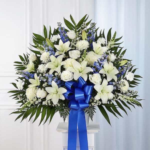 White lilies and roses with blue accents in a standing spray with a blue ribbon