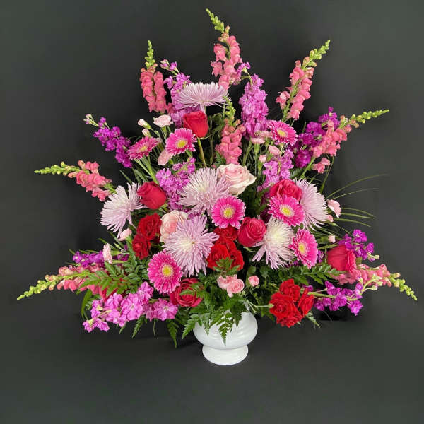 Large pink and red floral arrangement in a white vase